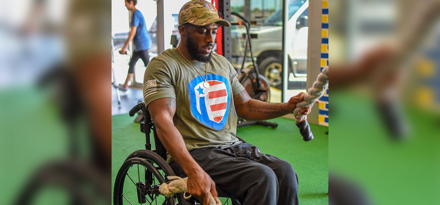 A veteran member in a wheelchair and a camo cap works battle ropes.