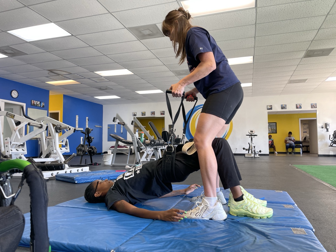 A trainer helps a member hold a bridge on the mats.